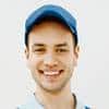 A young man wearing a blue cap and light blue shirt smiling at the camera against a plain white background.